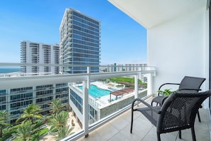 A balcony with a view of a swimming pool, a high-rise building, and a clear blue sky. - Private Residence at Carillon Resort - 910 (Miami Beach)