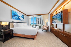 A hotel room with a large bed, a TV, a desk with a lamp, a chair, and a view of the cityscape. - Private Residence at Carillon Resort - 910 (Miami Beach)