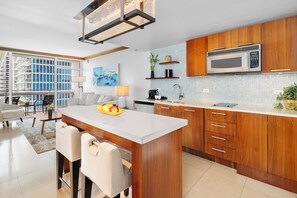 A modern kitchen with wooden cabinets, a stainless steel microwave, and a fruit bowl on the island. - Private Residence at Carillon Resort - 910 (Miami Beach)