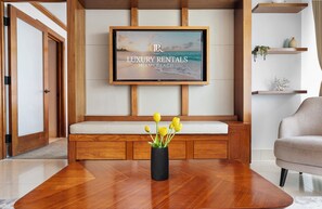 Ein modernes Wohnzimmer mit einer Holzbank, einem an der Wand befestigten Flachbildfernseher und einem Couchtisch mit einer Vase voller gelber Blumen.