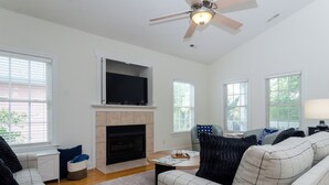 A living room with a fireplace, a ceiling fan, and a flat-screen TV mounted above it. - Inviting Single Family Home Near Beach - K403 (Kure Beach)