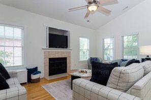 A living room with a fireplace, a ceiling fan, and a flat-screen TV mounted above it. - Inviting Single Family Home Near Beach - K403 (Kure Beach)