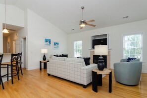 Un salon comprenant un canapé, un fauteuil, une table à manger, des chaises, un ventilateur de plafond et des œuvres d’art accrochées aux murs.