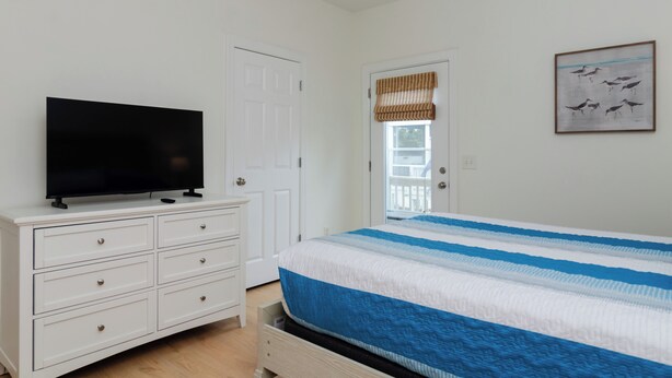 A bedroom with a bed, a television on a dresser, a door, and a window with a view. - Inviting Single Family Home Near Beach - K403 (Kure Beach)