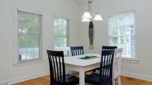 A dining area with a white table and blue chairs, three windows with blinds, and a hanging light fixture. - Inviting Single Family Home Near Beach - K403 (Kure Beach)