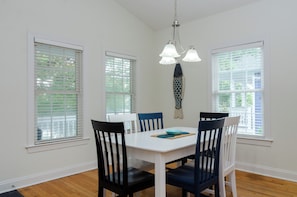 A dining area with a white table and blue chairs, three windows with blinds, and a hanging light fixture. - Inviting Single Family Home Near Beach - K403 (Kure Beach)