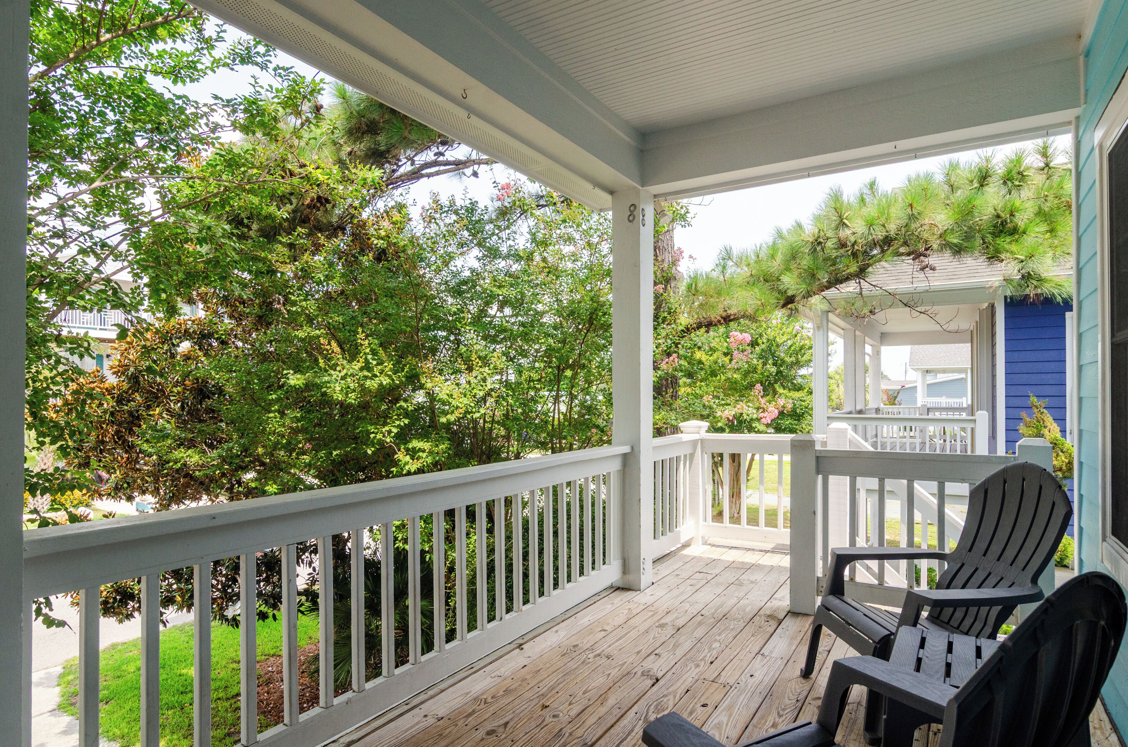 Une véranda couverte avec des balustrades blanches, une terrasse en bois et deux fauteuils Adirondack.