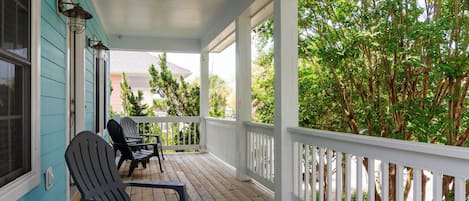 A covered porch with wooden flooring, two Adirondack chairs, and a white railing.