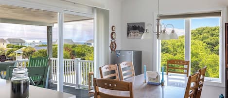 A dining area with a table and chairs, a refrigerator, and a view of greenery and houses.