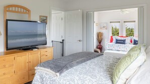 Un dormitorio con cama, televisor sobre una cómoda de madera y vista al exterior por una puerta abierta.