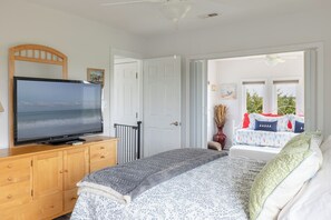 Ein Schlafzimmer mit einem Bett, einem Fernseher auf einer Holzkommode und Blick ins Freie durch eine geöffnete Tür.