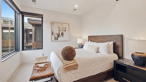 Een moderne slaapkamer met een groot bed, een bankje, een nachtkastje en een raam met uitzicht.
