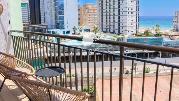 Ein Balkon mit Korbmöbeln, Blick auf den Strand und hohe Gebäude.