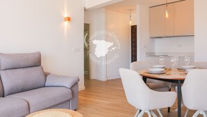 Ein modernes Wohnzimmer mit einer Couch, einem Esstisch mit Stühlen und einer Küchenzeile mit Schränken und einer Hängelampe.