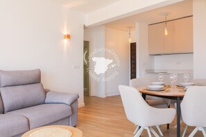Ein modernes Wohnzimmer mit einer Couch, einem Esstisch mit Stühlen und einer Küchenzeile mit Schränken und einer Hängelampe.