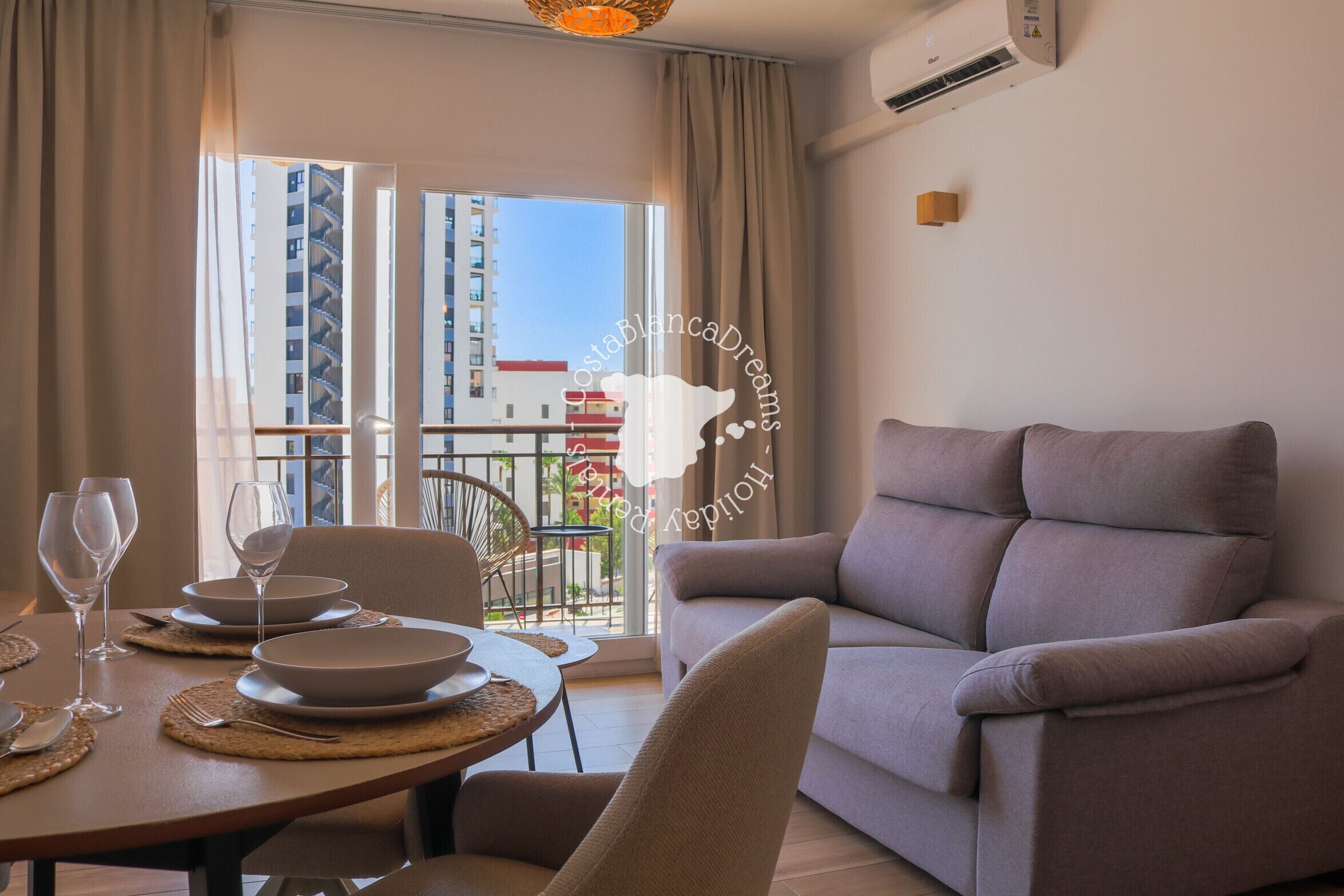 Ein modernes Wohnzimmer mit Sofa, Esstisch für zwei Personen und einem Balkon mit Blick auf Gebäude.