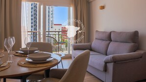 Ein modernes Wohnzimmer mit Sofa, Esstisch für zwei Personen und einem Balkon mit Blick auf Gebäude.