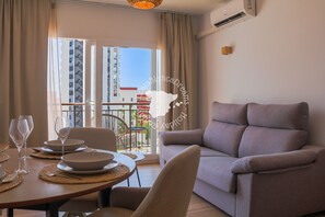 Ein modernes Wohnzimmer mit Sofa, Esstisch für zwei Personen und einem Balkon mit Blick auf Gebäude.