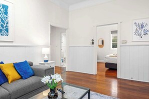 Relax on the plush grey sofa, styled with cheerful pops of bright yellow and electric blue pillows, situated next to a modern glass-top coffee table. - Classic Australian Charm (East Victoria Park)