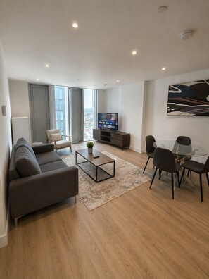 Uma sala de estar moderna com sofá, mesa de centro, televisão e área de jantar.