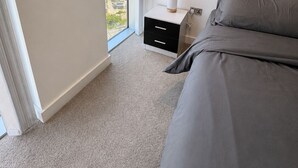 Quarto com uma janela grande, uma cama, mesa de cabeceira e vista para a cidade.