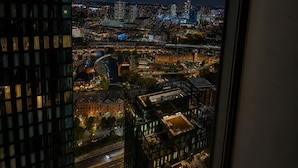 Vista noturna de um horizonte urbano, com janelas iluminadas e a área urbana visível abaixo.