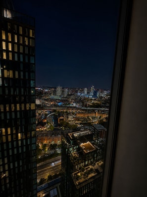 Nachtansicht einer Stadtlandschaft von einem Hochhaus aus, mit beleuchteten Fenstern und Blick auf das darunterliegende Stadtgebiet.