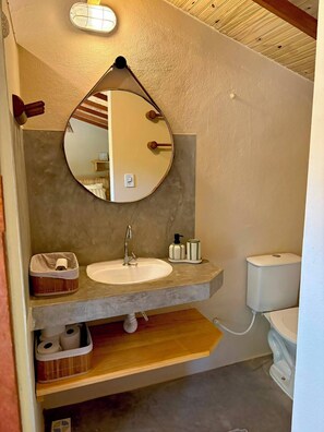 Ein Badezimmer mit rundem Spiegel, Waschbecken, Toilette und Ablagefläche für Pflegeprodukte.