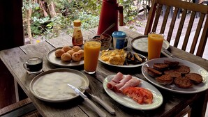 A wooden table with breakfast items, a red thermos, and a glass of orange juice. - Cozy, comfy house in the heart of Caraíva - fully equipped and peaceful located (Caraíva)