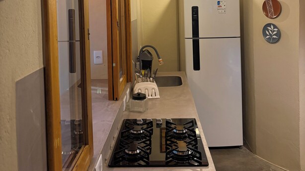 A kitchen with a stove, refrigerator, and a hanging light fixture. - Cozy, comfy house in the heart of Caraíva - fully equipped and peaceful located (Caraíva)