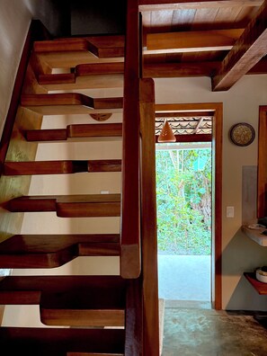 Eine Holztreppe führt zu einer Tür, durch die grünes Laub sichtbar ist.