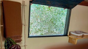 A room with a wooden ceiling, a window with a view of trees, a bed with a striped bedspread, and a plant in a woven basket. - Cozy, comfy house in the heart of Caraíva - fully equipped and peaceful located (Caraíva)
