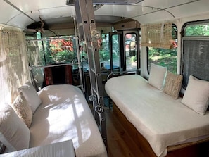 A compact, well-lit interior with two beds, a ladder, and a window providing a view of greenery outside. - Rooftop bus, outdoor shower + bathtub (dry toilet) (Mimizan)
