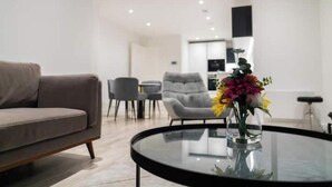 A modern living room with a sofa, a glass coffee table with a vase of flowers, and a dining area with chairs and a table. - Modern 2-Bed Penthouse in Deansgate | Stunning City Views (Manchester)