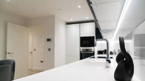 A modern kitchen with white cabinetry, a built-in oven, and a black kettle on the counter. - Modern 2-Bed Penthouse in Deansgate | Stunning City Views (Manchester)