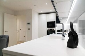 Eine moderne Küche mit weißen Schränken, einem eingebauten Ofen und einem schwarzen Wasserkocher auf der Arbeitsfläche.