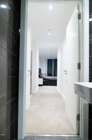 A hallway leading to a bedroom with a bed, a nightstand, and a window. - Modern 2-Bed Penthouse in Deansgate | Stunning City Views (Manchester)