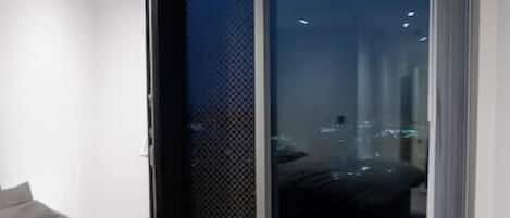 A modern bedroom with a large bed, a sliding glass door leading to a balcony, and a city view.