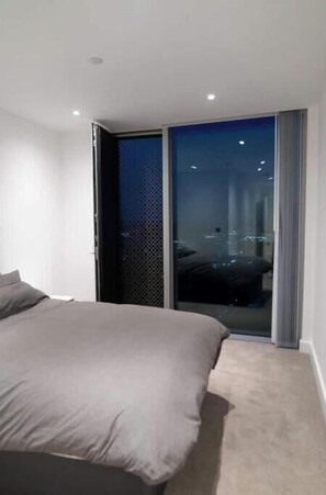 Ein modernes Schlafzimmer mit einem großen Bett, einer Schiebetür zu einem Balkon und Blick auf die Stadt.