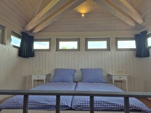 Ein Zimmer mit einem Bett, zwei Nachttischen und drei mit Vorhängen versehenen Fenstern.