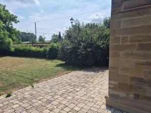 Ein gepflasterter Außenbereich mit Backsteinmauer, Pflanzen und einem entfernten Zug.