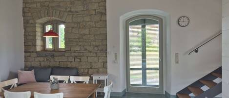 A dining area with a stone wall, a wooden ceiling, a dining table with chairs, a sofa, and a staircase.