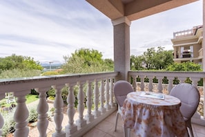 Un balcon doté d’une balustrade blanche, une table ronde recouverte d’une nappe à motifs floraux et deux chaises.