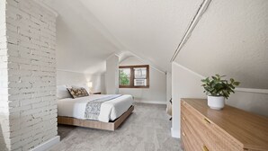 A bedroom with a loft-style ceiling, a bed, a wooden dresser, and a potted plant. - MINNeSTAY* Magnolia House (Minneapolis)