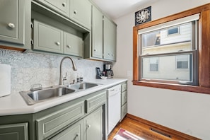 A kitchen with two sinks, a dishwasher, and a window overlooking a residential area. - MINNeSTAY* Magnolia House (Minneapolis)