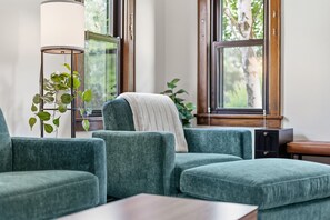 Een moderne woonkamer met een zithoek, een vloerlamp en uitzicht op bomen door grote ramen.