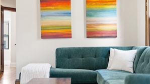 A living room with a green sofa, a white pillow, and two abstract paintings on the wall. - MINNeSTAY* Magnolia House (Minneapolis)