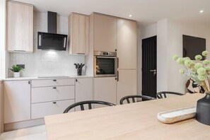Eine moderne Küche mit hellen Holzschränken, einer eingebauten Mikrowelle, einem Backofen und einem Essbereich mit Tisch und Stühlen.