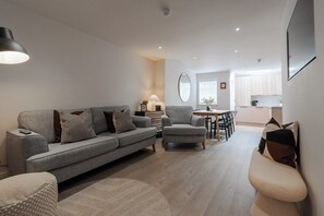 Un salon moderne avec un canapé gris, des fauteuils et un coin repas à l’arrière-plan.