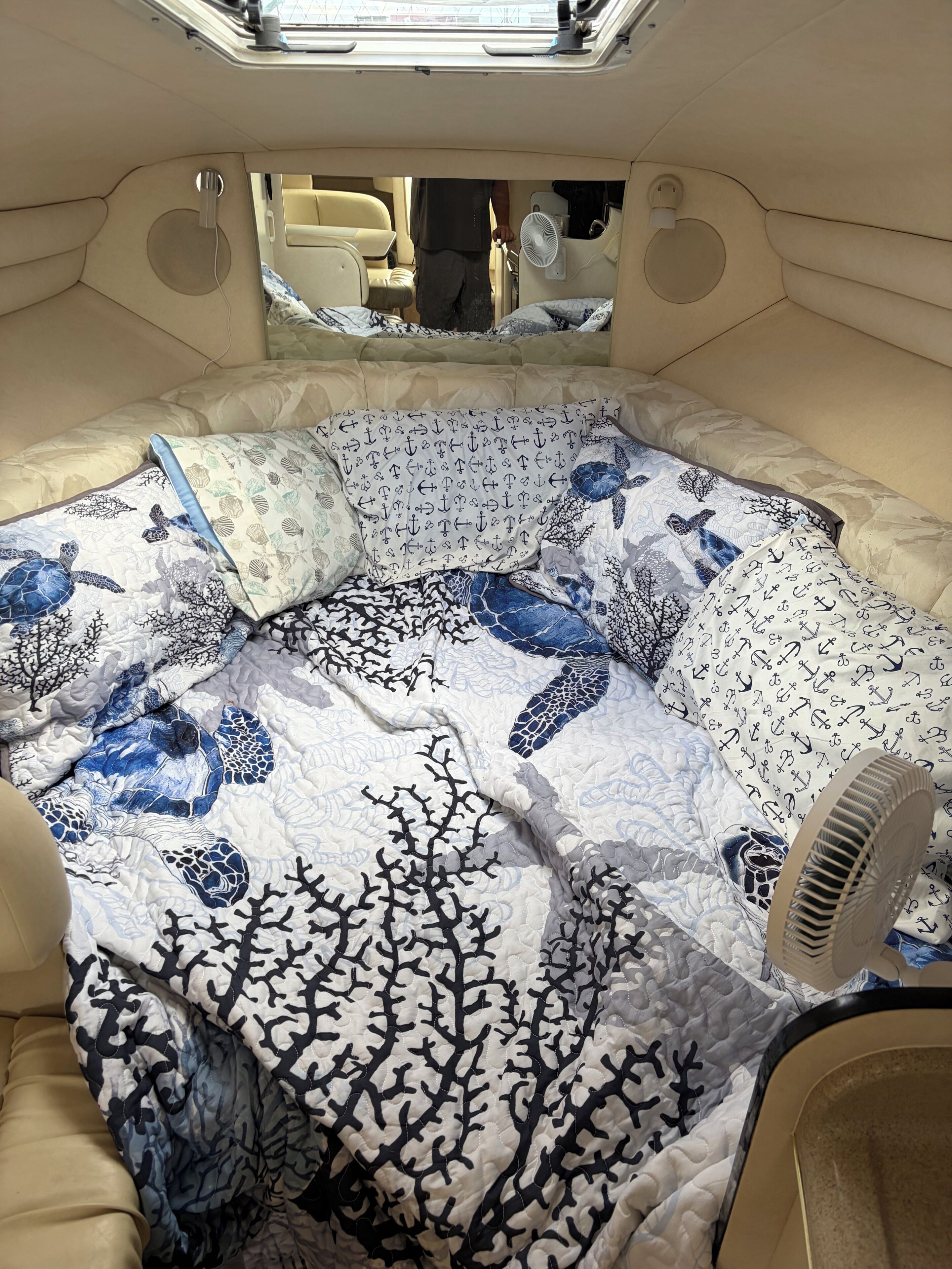 A bed with a patterned bedspread, a fan, and a window above.